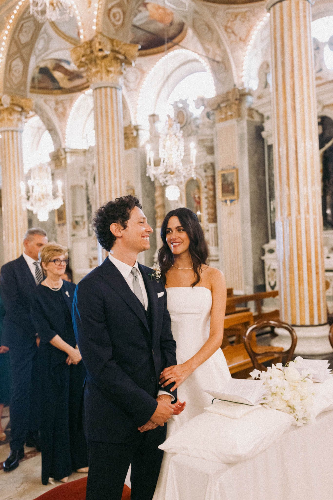 Elegant wedding ceremony inside an ornate baroque church with gilded columns and arched ceilings.