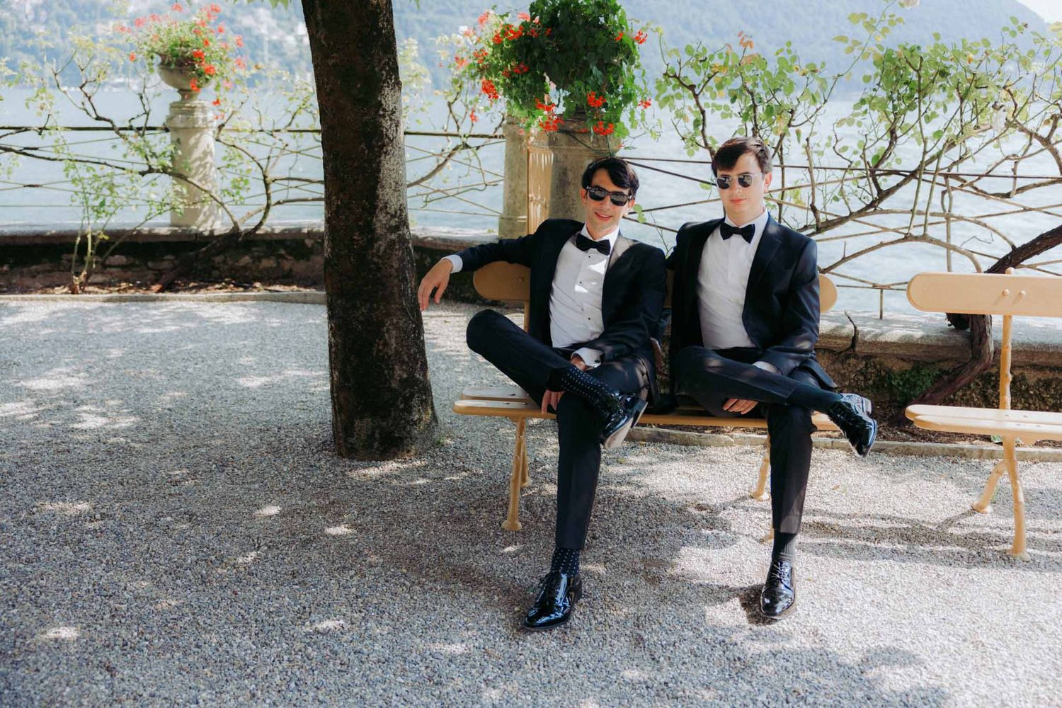 A sequence of black dress shoes stepping across a gravel path in a garden setting.
