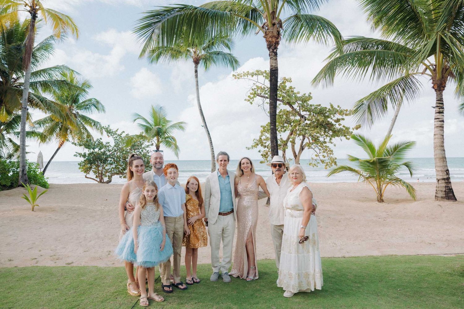 Palm trees line a tropical beach as people gather for a destination wedding ceremony at sunset.