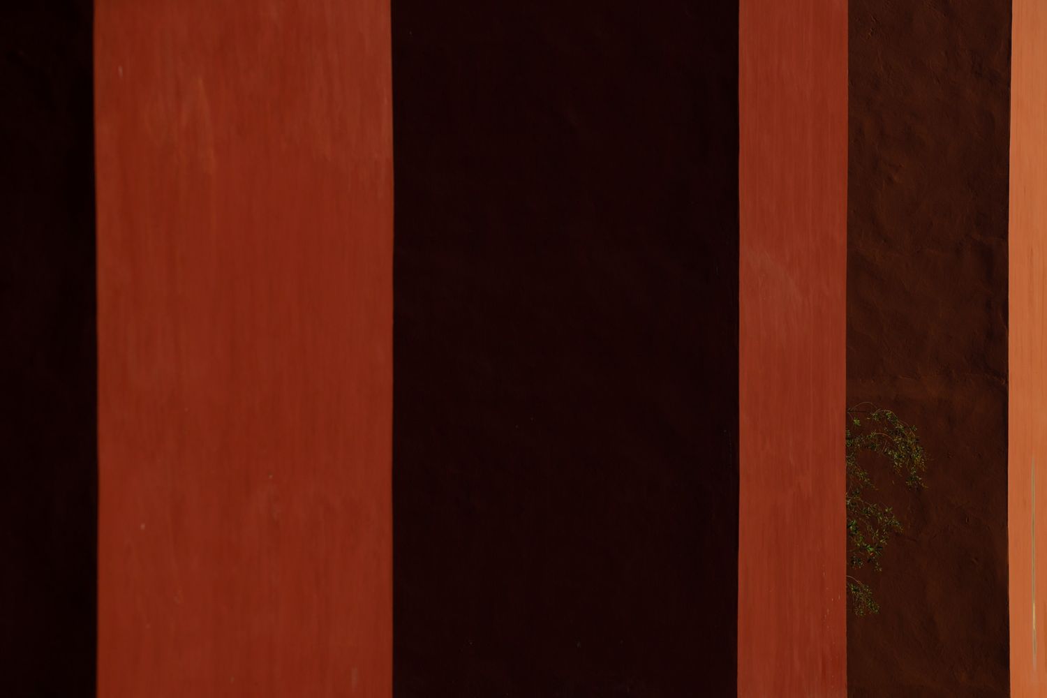 Geometric pattern of dark shadows cast by vertical pillars against a terracotta colored wall.