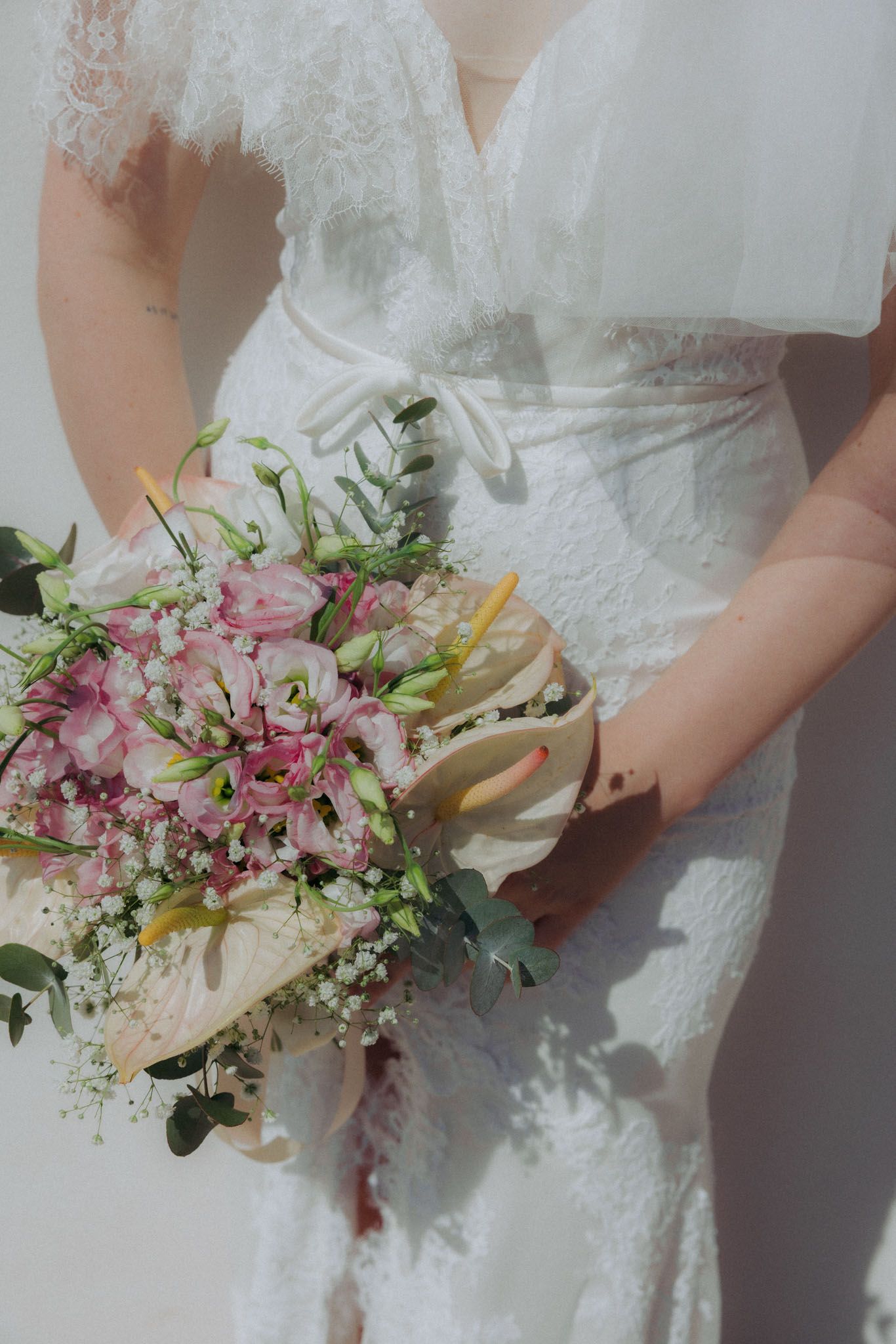 Close-up view of elegant bridal bouquet featuring pink lilies, white calla lilies and delicate greenery.