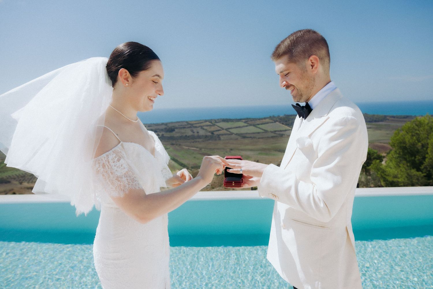 A couple shares a joyful moment during their wedding ceremony against a stunning coastal backdrop with blue waters.