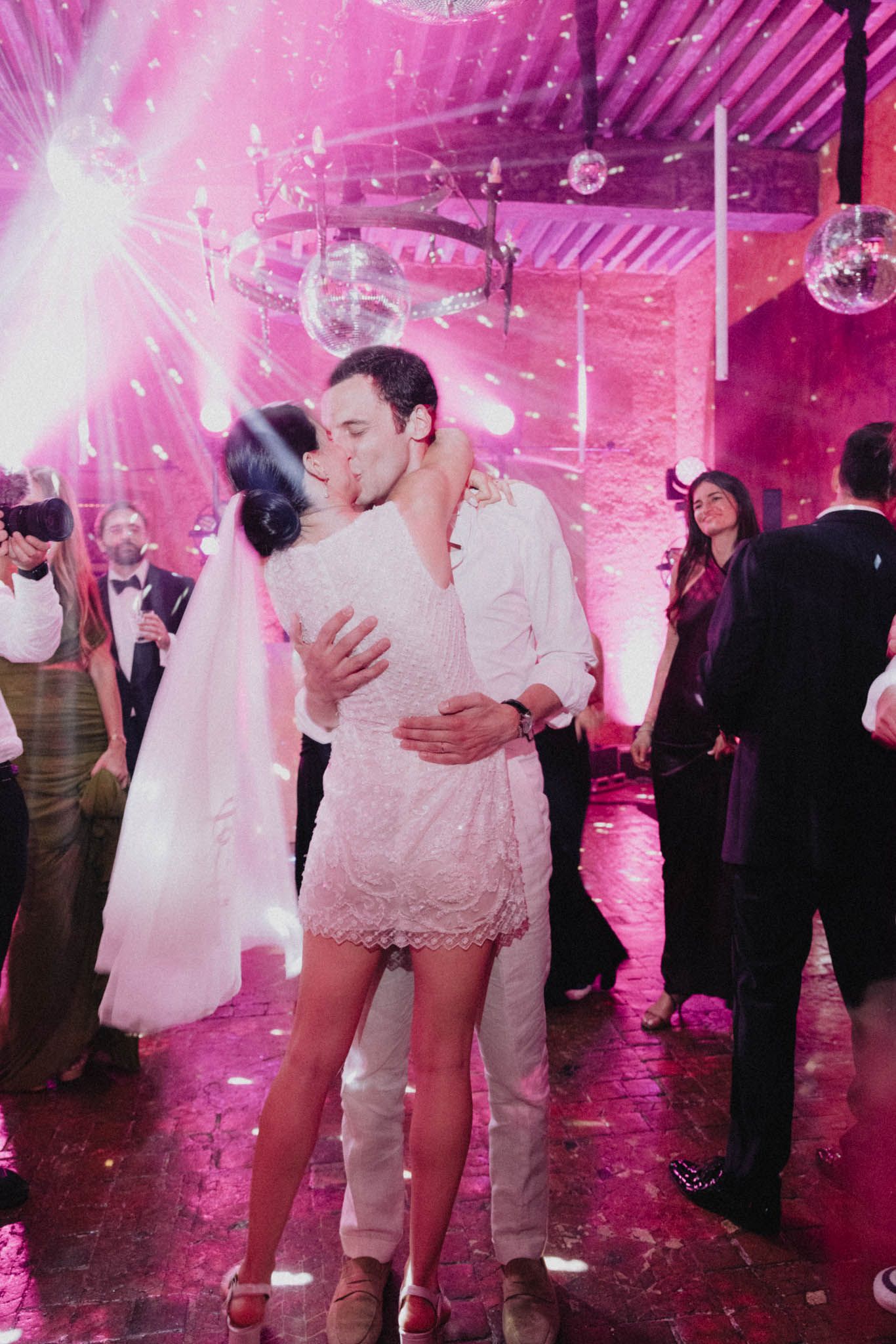 Couples dancing under pink disco lights and mirror balls at an elegant wedding reception venue.