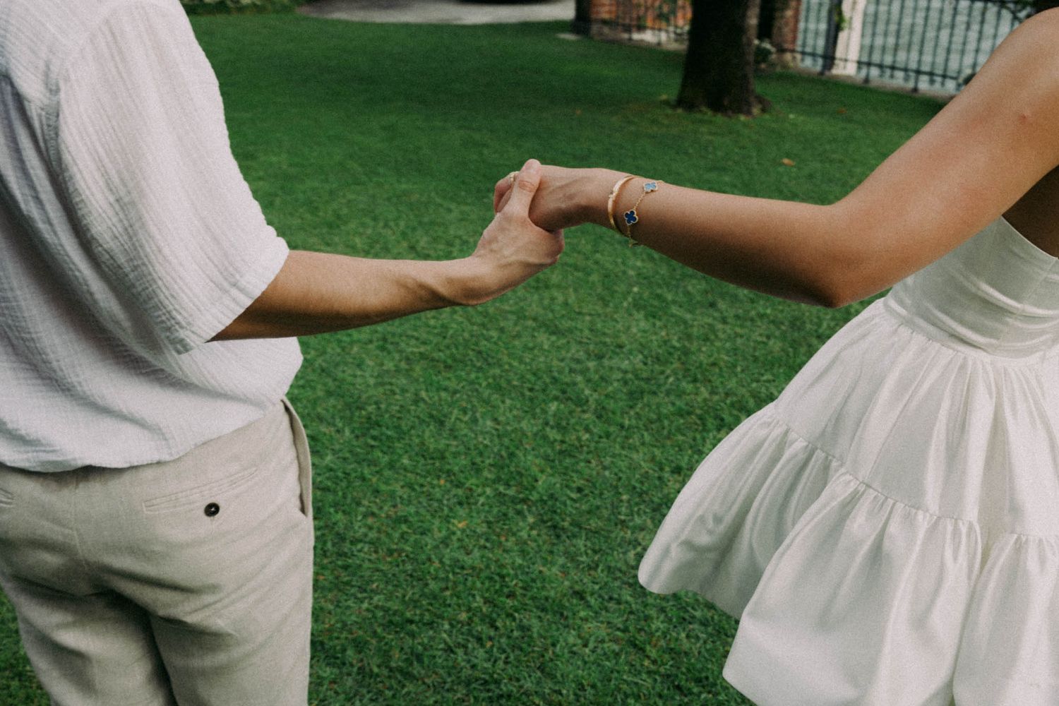 A couple in white clothing poses together on green grass during a photo session.
