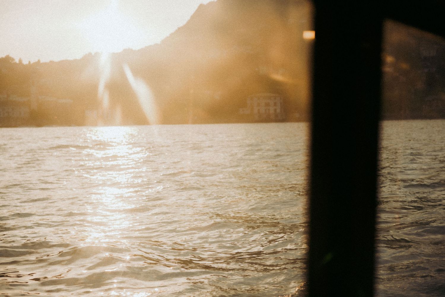 A serene panoramic view of a sunset over a lake with silhouetted trees and mountains in the background.