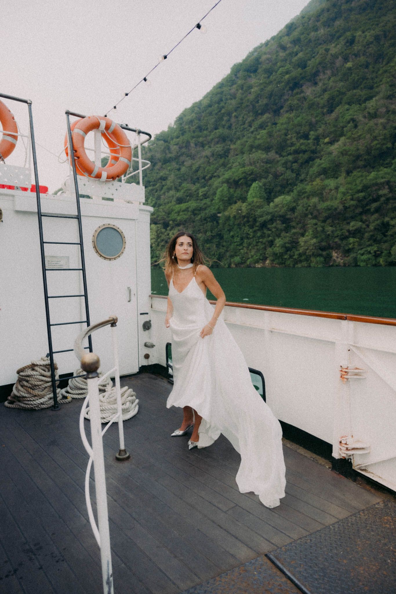A sequence of photos showing a person in a white dress dancing on a boat deck with mountains in the background.