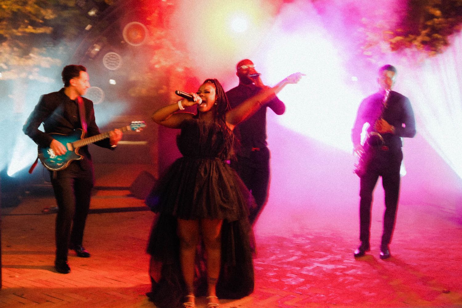 Musicians perform on stage with dramatic red and pink lighting effects creating an atmospheric concert environment.