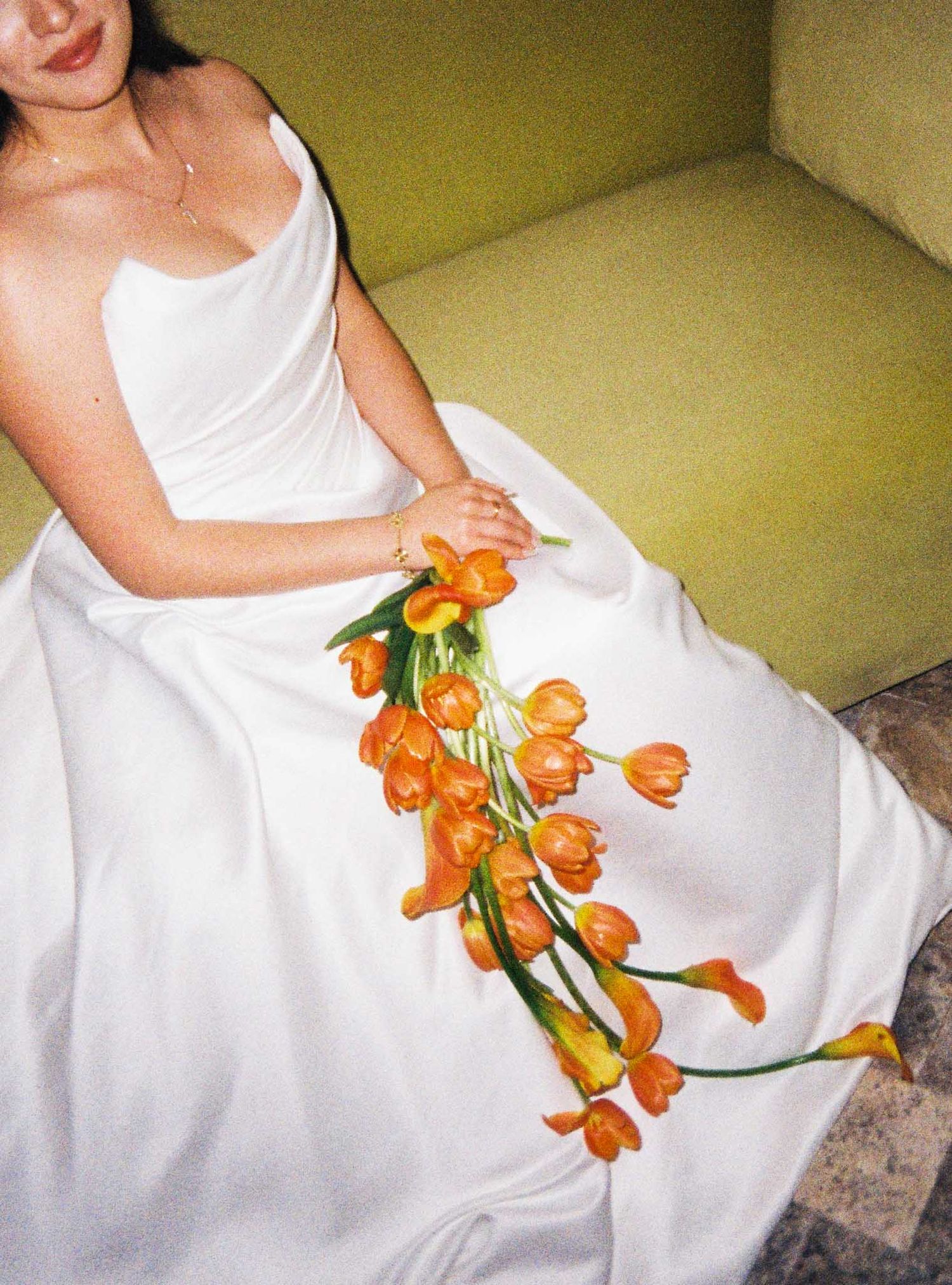A person in a white dress holds vibrant orange tropical flowers while sitting on a yellow couch.