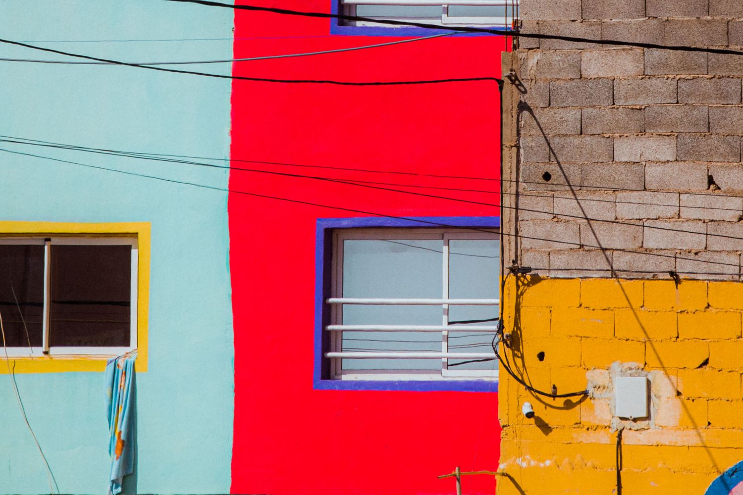 Colorful geometric wall mural featuring bright red, turquoise, and yellow blocks painted on a brick building facade.