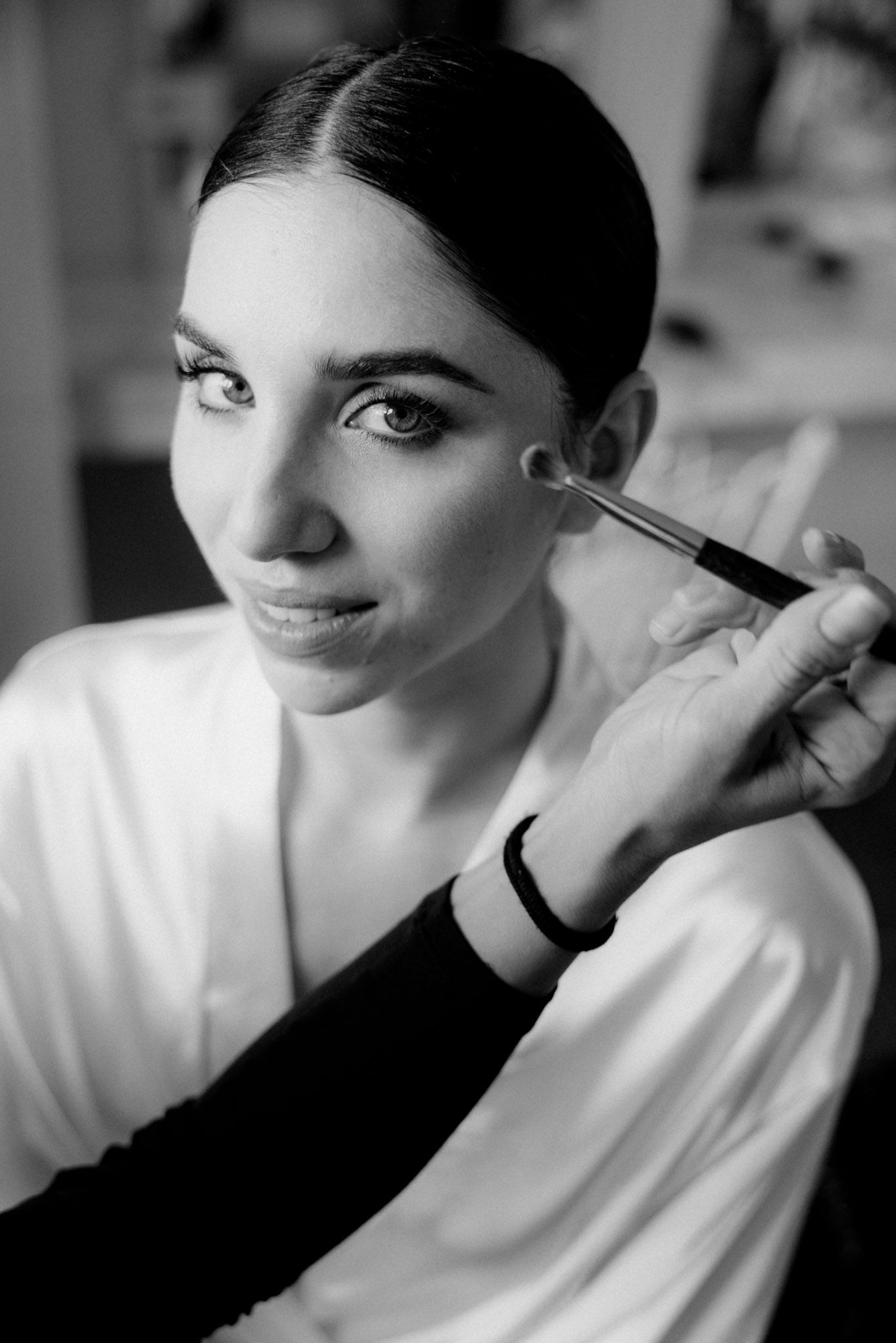 Black and white photo sequence showing makeup being applied with brushes in a professional beauty session.