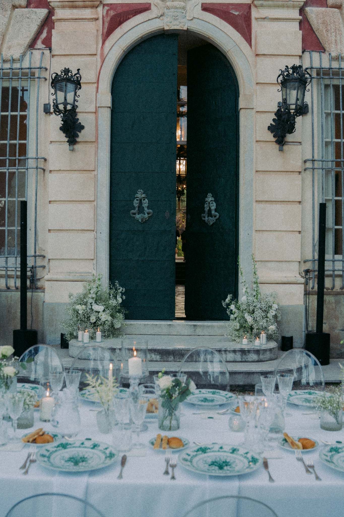 Elegant wedding reception table setting with white linens, floral centerpieces and ornate architecture in the background.