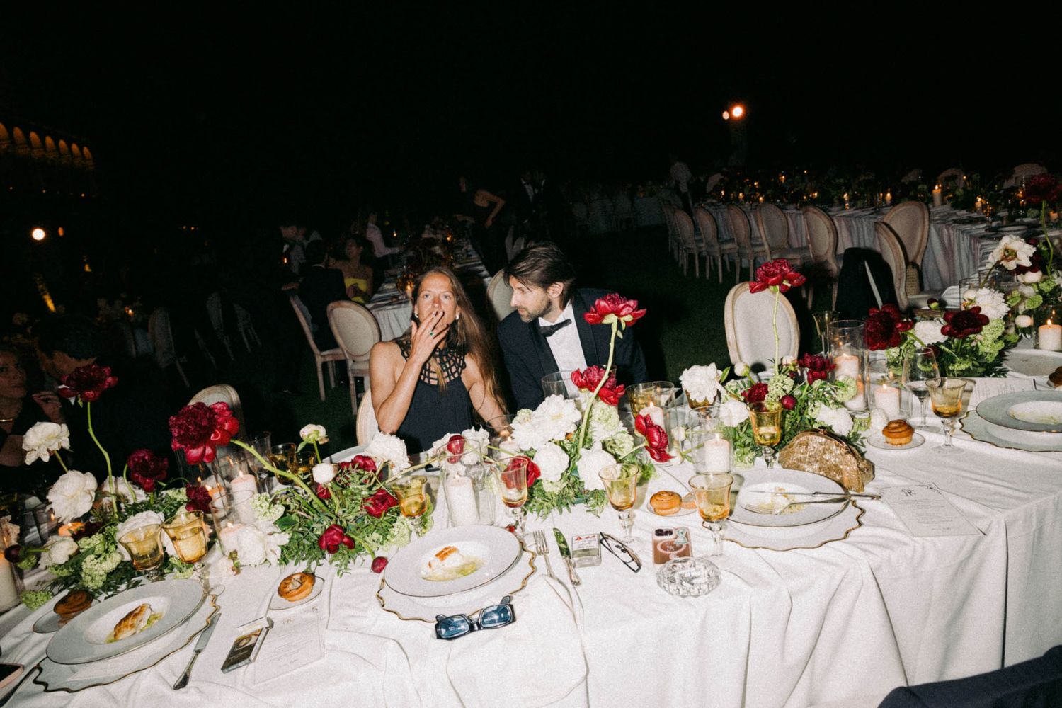 Elegant dinner party table decorated with floral centerpieces and place settings at night.
