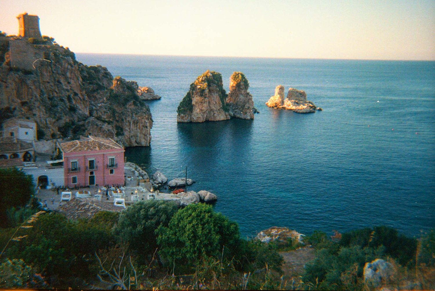 Scenic coastal view of Scopello, Sicily with dramatic rocky cliffs and turquoise Mediterranean waters at sunset.