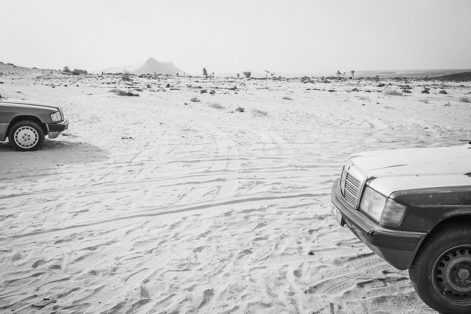 Desert landscape with multiple vehicles parked on sandy terrain under a bright sky.