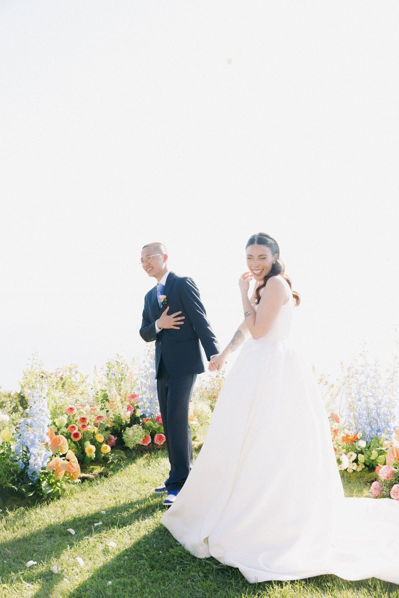 A couple in wedding attire dances joyfully in a garden filled with colorful summer flowers.