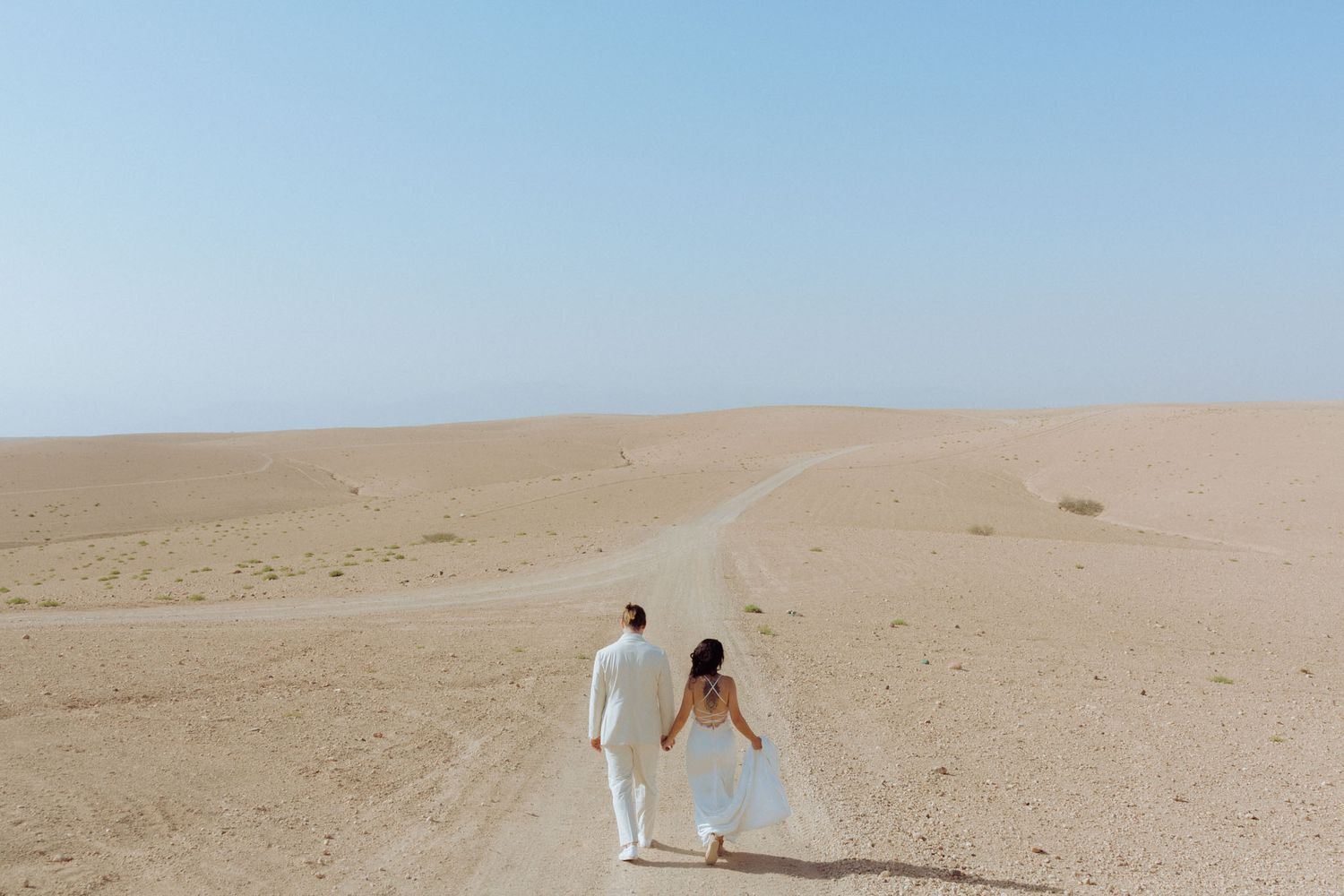 A white horse and rider traverse a vast sandy desert landscape under bright blue skies.