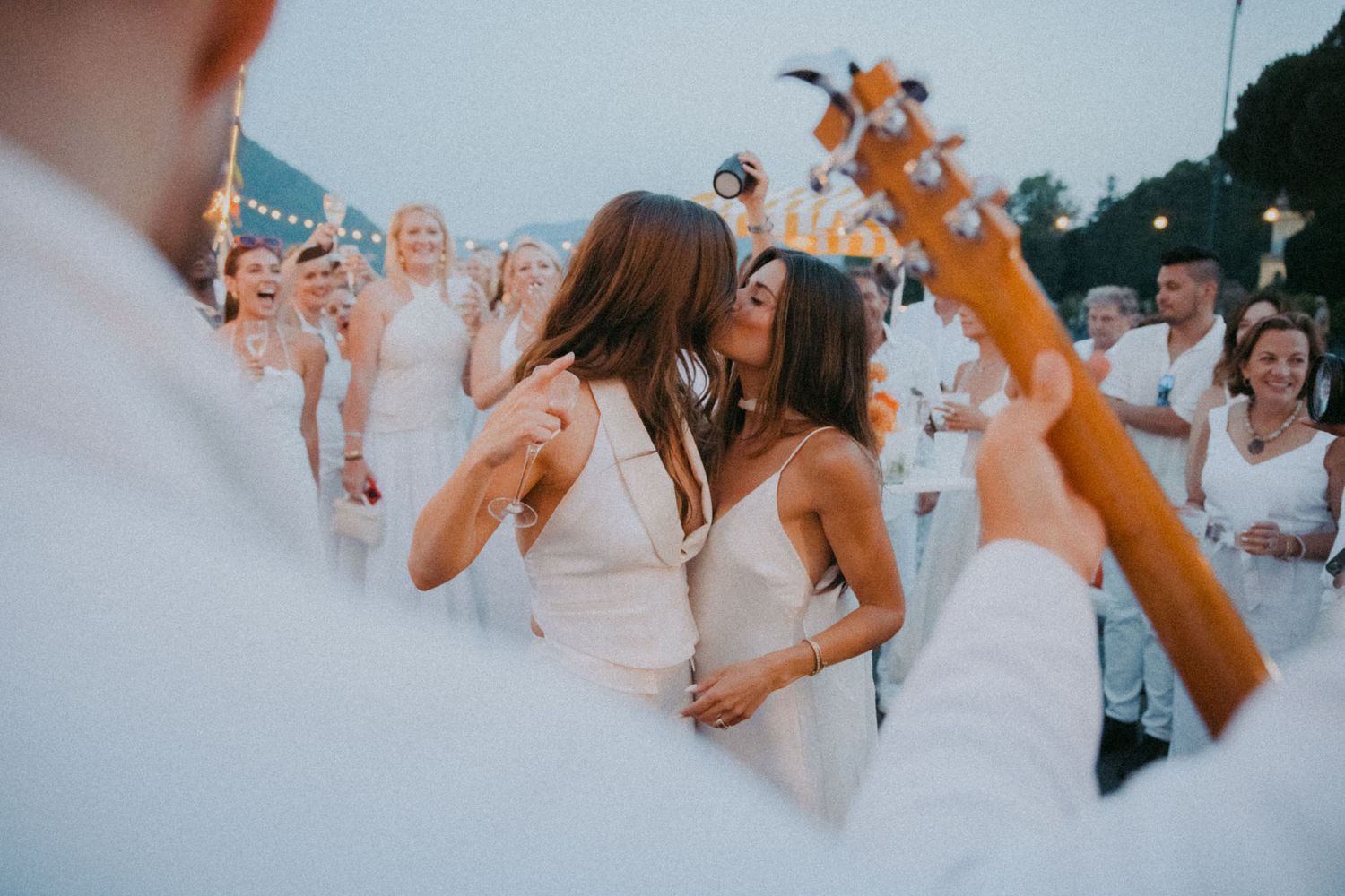 A group of wedding guests dance together at an outdoor reception during sunset.