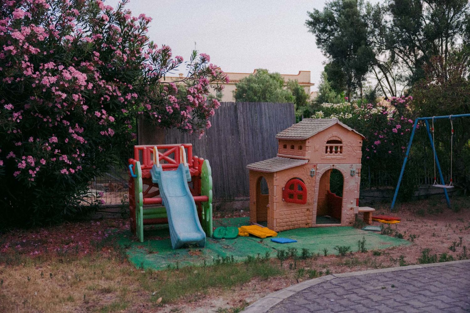 Colorful playground equipment including swings and slides set up in a backyard with pink flowering trees.
