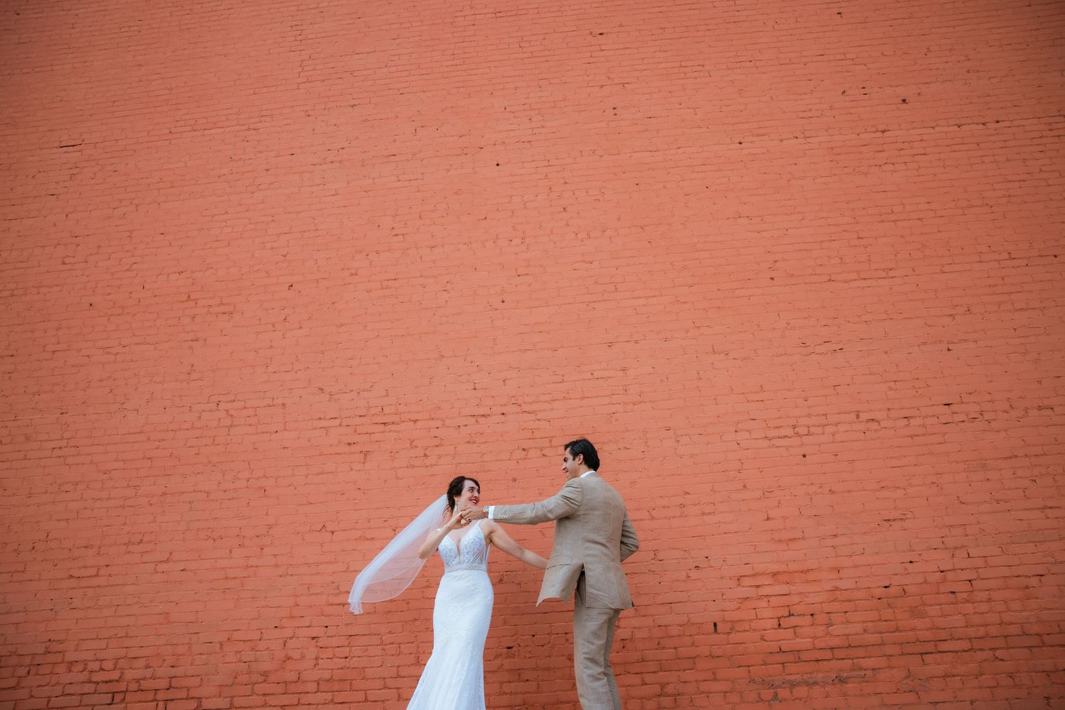 Two dancers perform an expressive contemporary dance routine against a rustic brick wall backdrop.