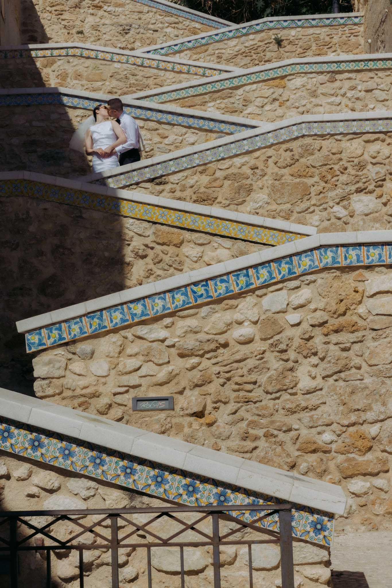 Decorative blue and white ceramic tiles line a curved stone staircase with metal railings in an outdoor setting.