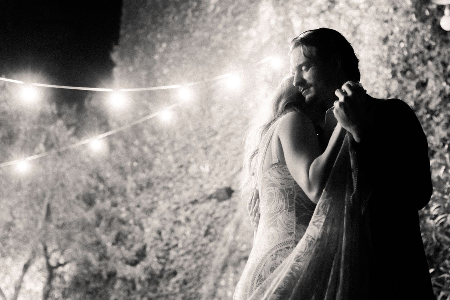 A black and white photo series showing a couple in romantic poses under string lights in an outdoor setting.