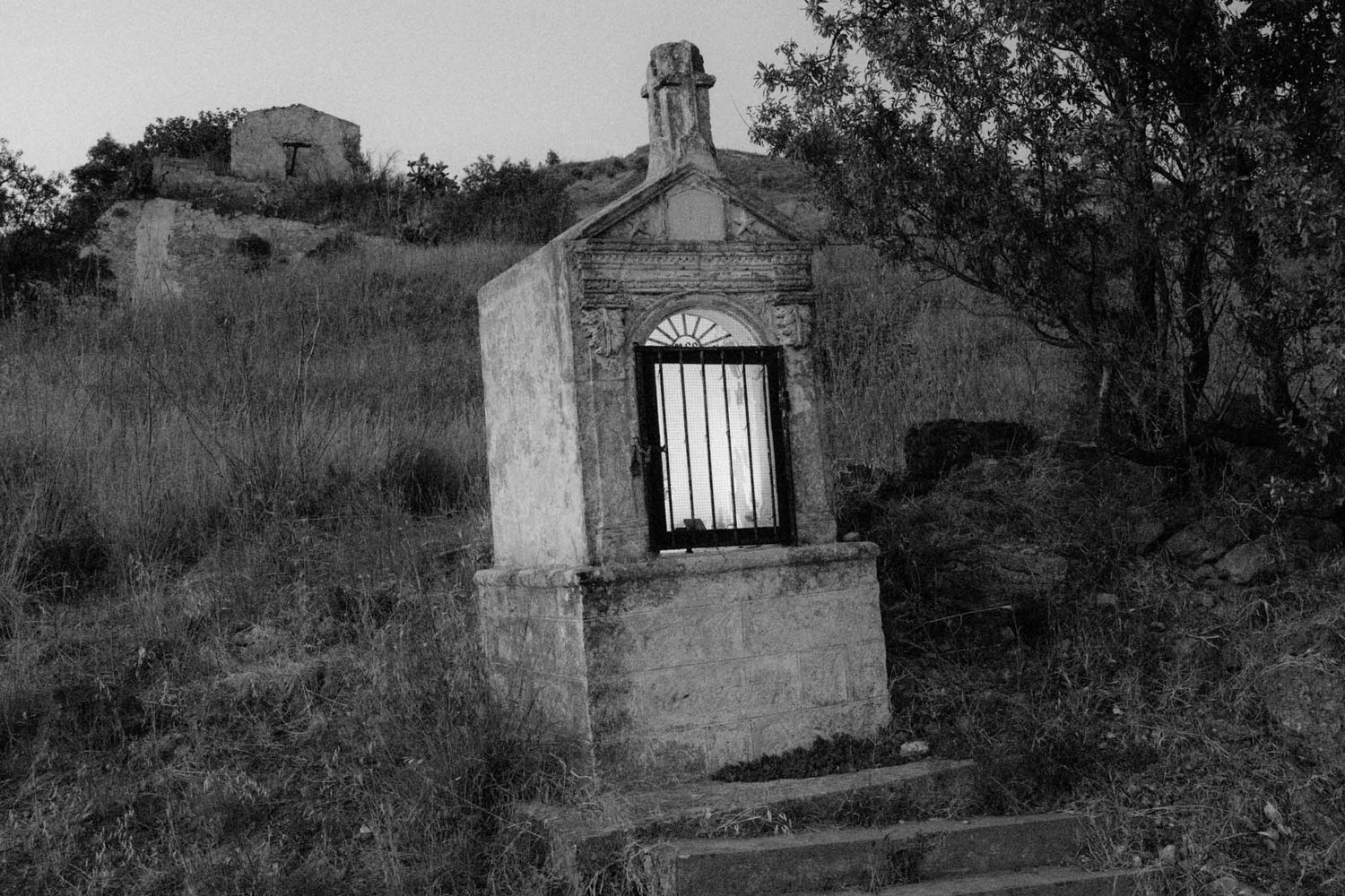Abandoned stone buildings and ruins scattered across a rural hillside landscape in black and white.