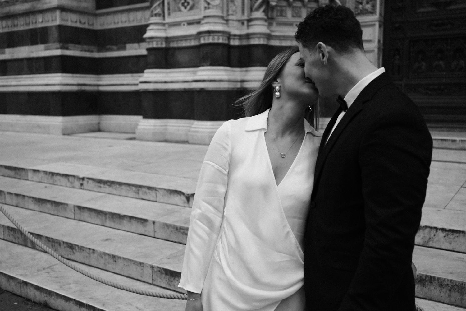 A romantic black and white wedding photo series showing a couple embracing on stone steps.