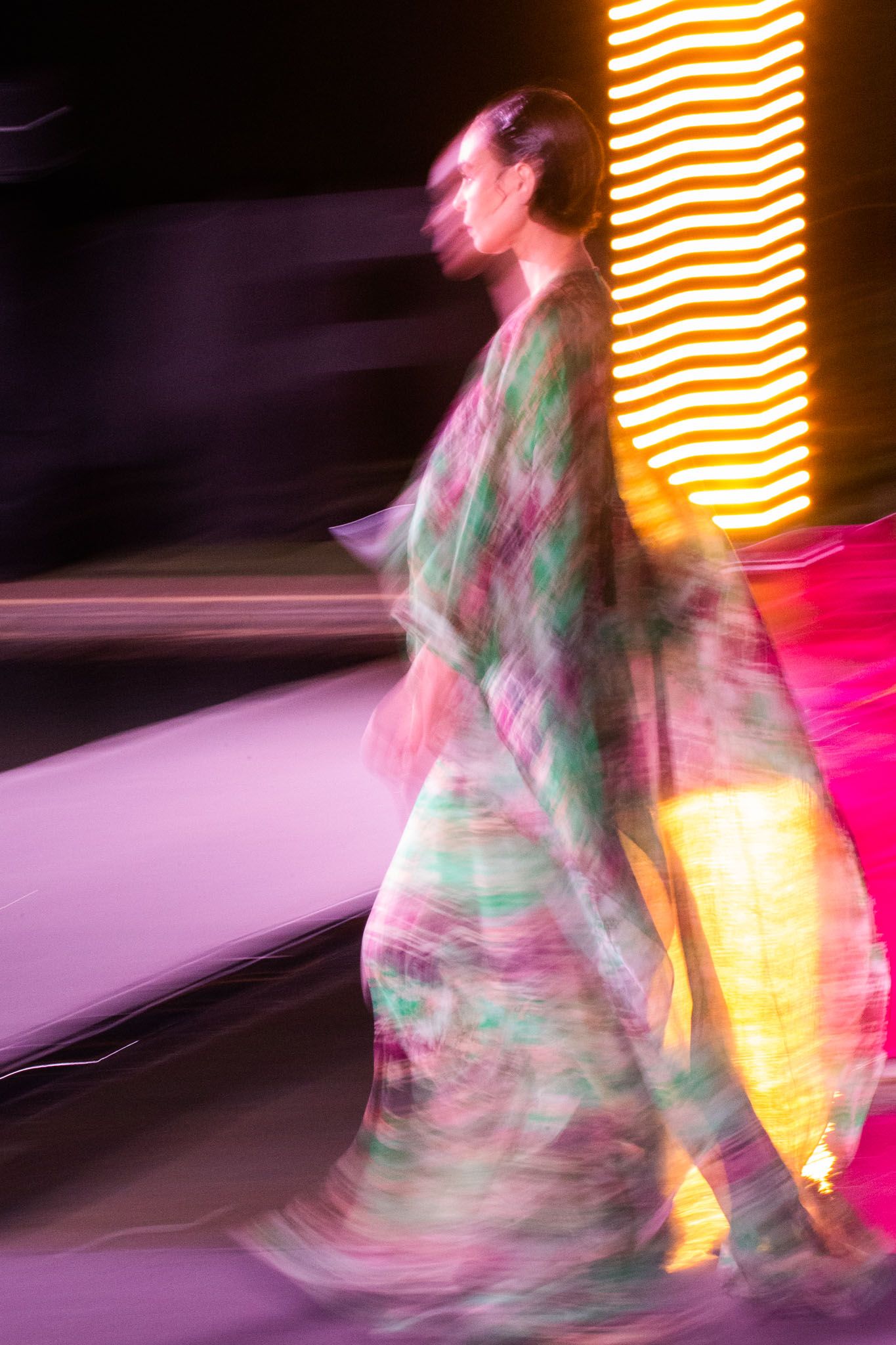 Motion blur photograph of a figure in a dress dancing with orange neon lights creating an ethereal effect.