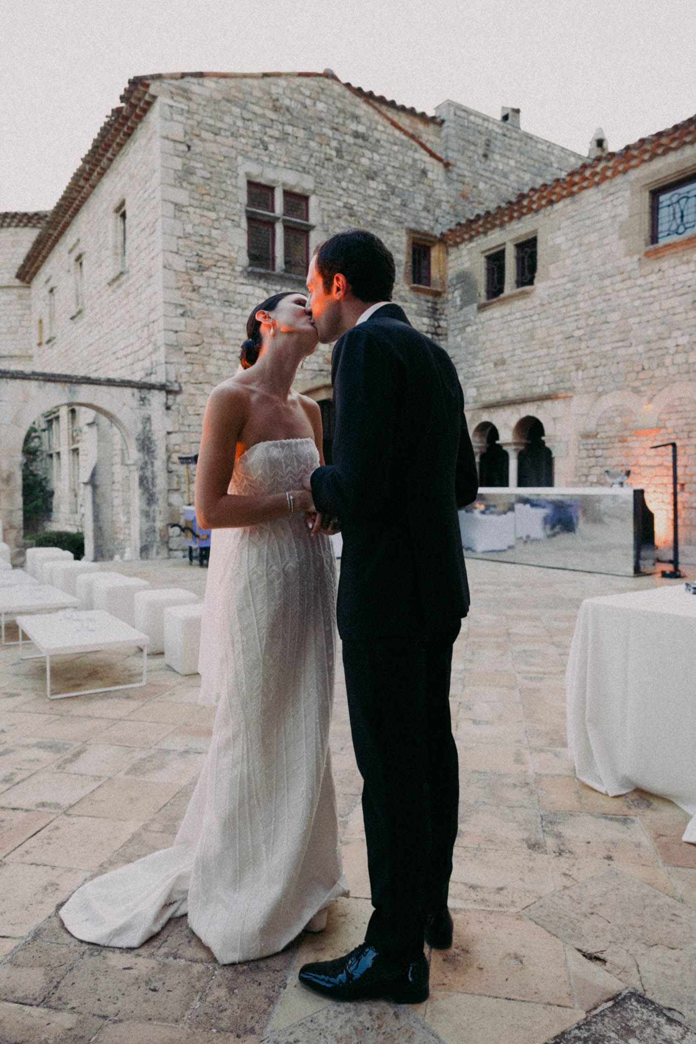 Wedding couple standing together on a stone terrace with rustic architecture in the background.
