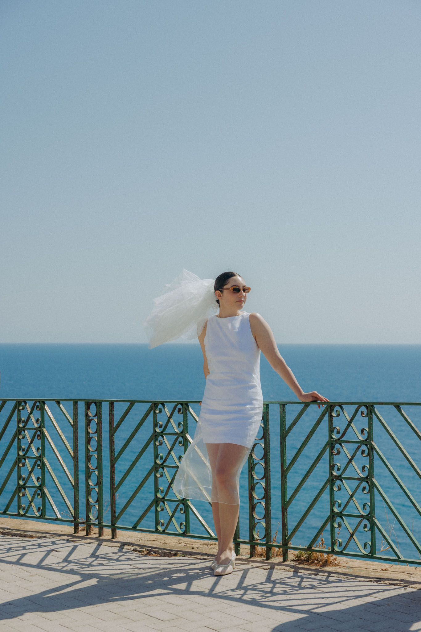 Person in white dress enjoying scenic ocean view from seaside balcony on bright sunny day.