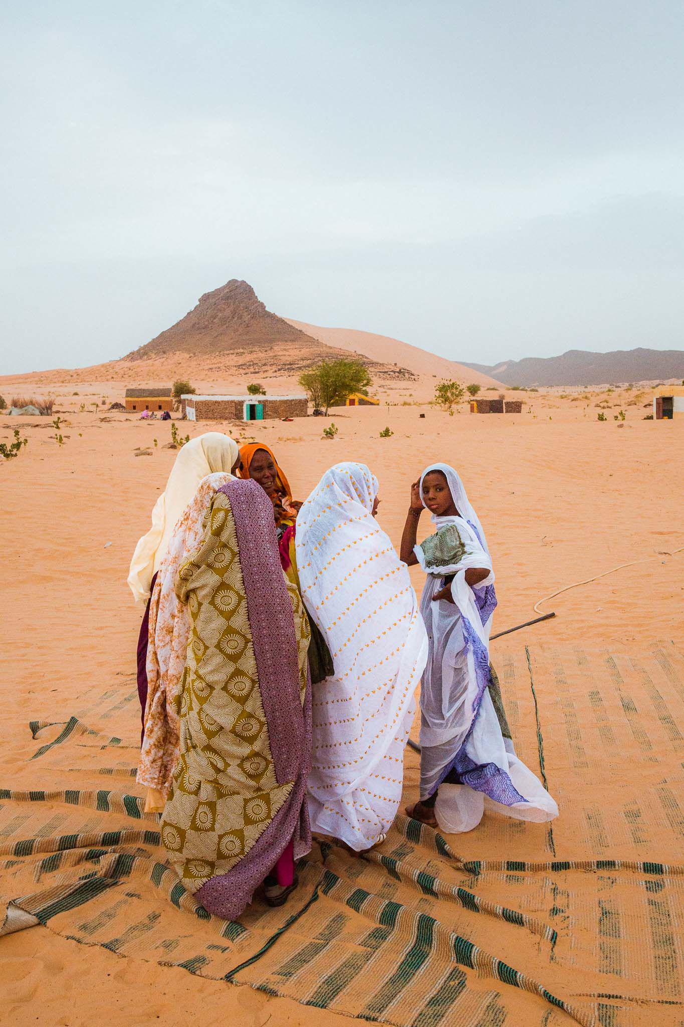Three figures in colorful traditional robes stand together against a desert mountain backdrop.