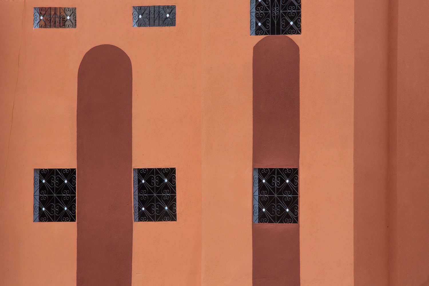 A terracotta-colored wall with arched architectural details and black decorative metal grilles mounted above.