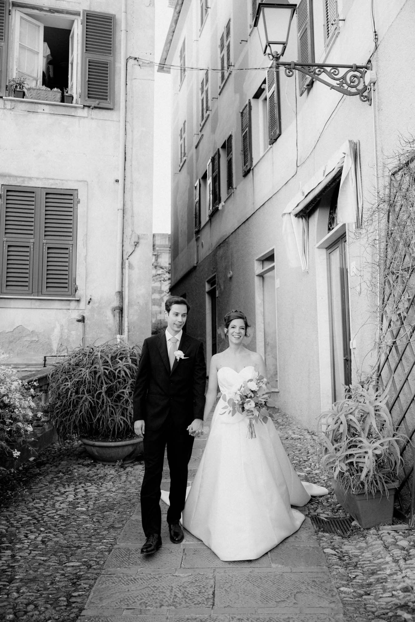 A black and white wedding photo series showing a couple walking along a charming cobblestone street in Europe.