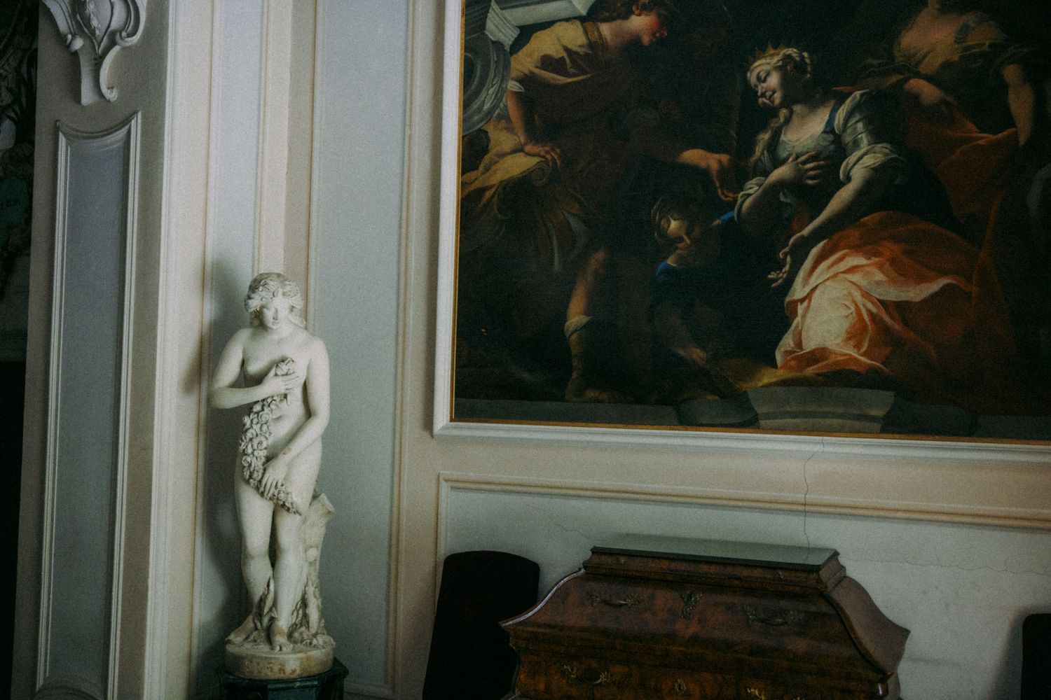 Classical white marble statue displayed next to a dark Renaissance painting in an ornate interior setting.