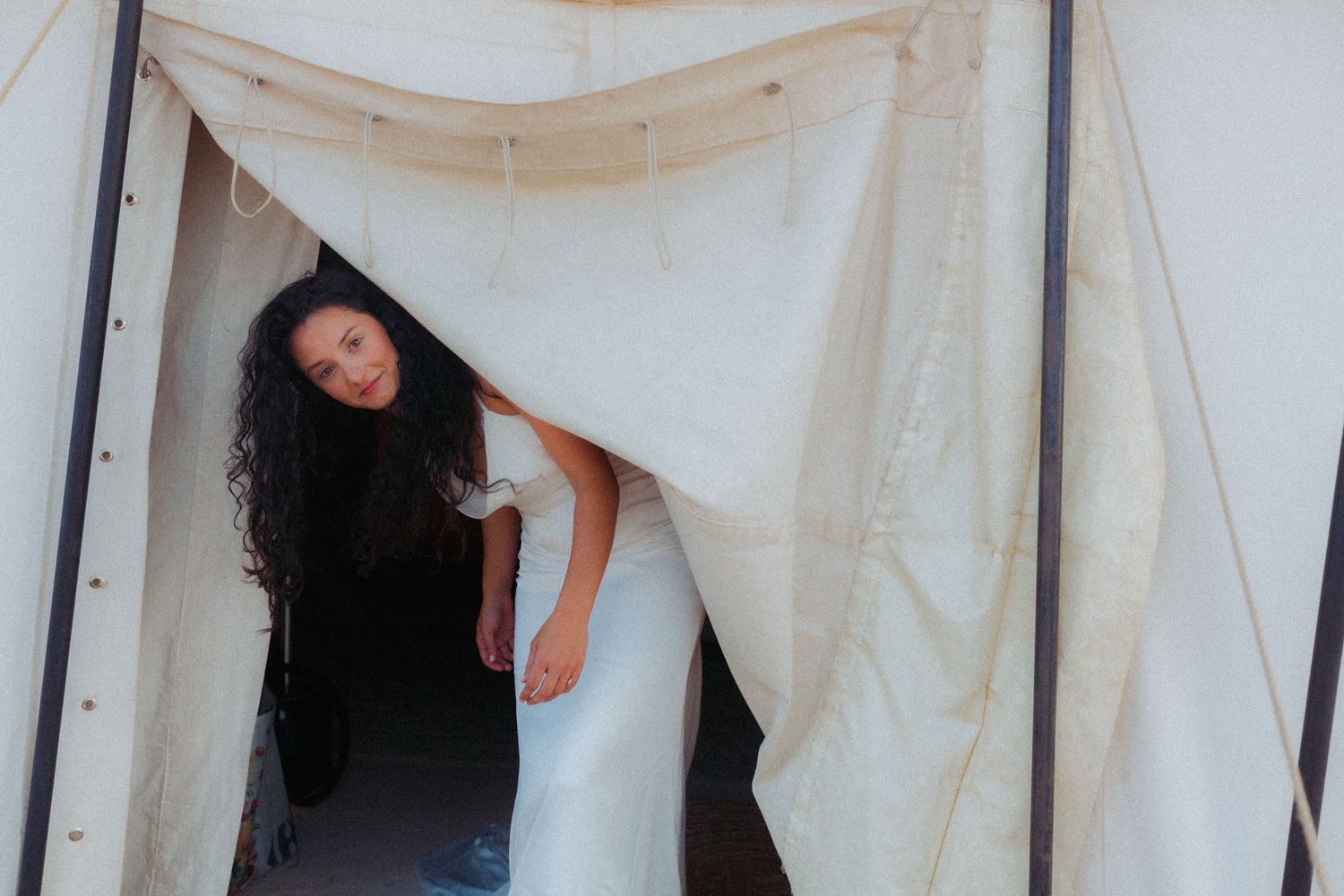 A figure emerges from behind a white curtain or fabric panel in an artistic installation or performance setting.