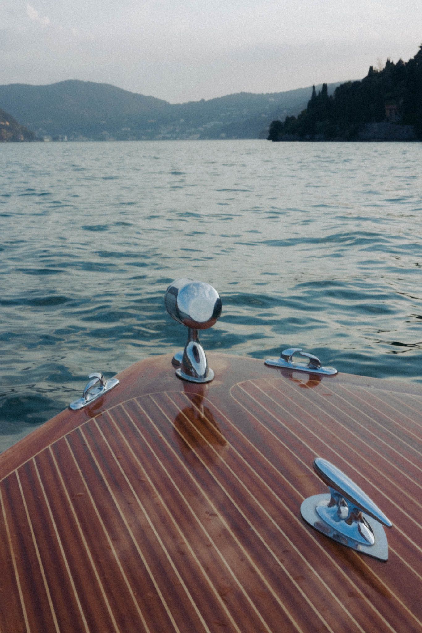 Seagulls perched on a wooden boat deck overlooking a serene mountain lake on a misty day.
