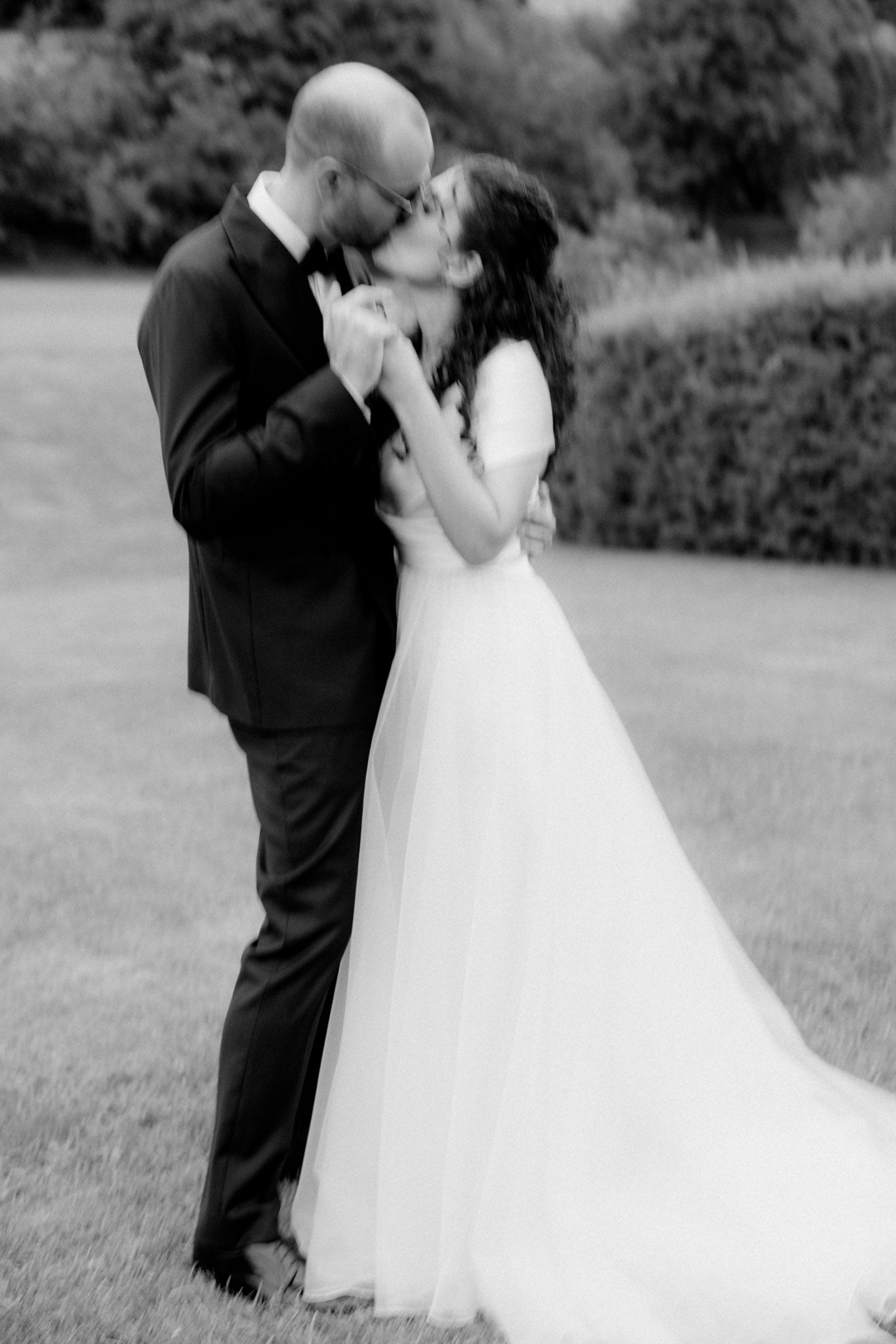 A romantic black and white wedding photo of a couple sharing a tender kiss in an outdoor garden setting.