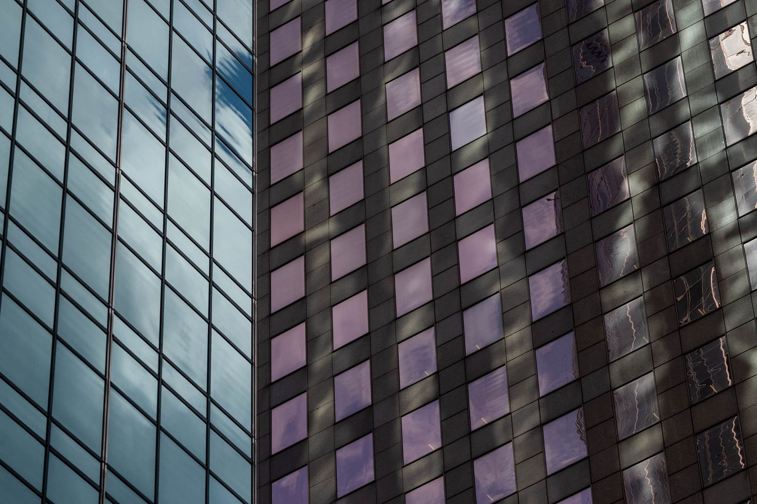 Modern glass office building facade with geometric patterns reflecting blue sky and clouds in its windows.