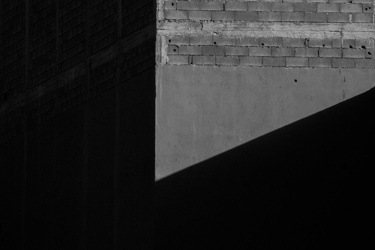 Architectural detail showing a dark corner intersection of brick walls with dramatic shadows.