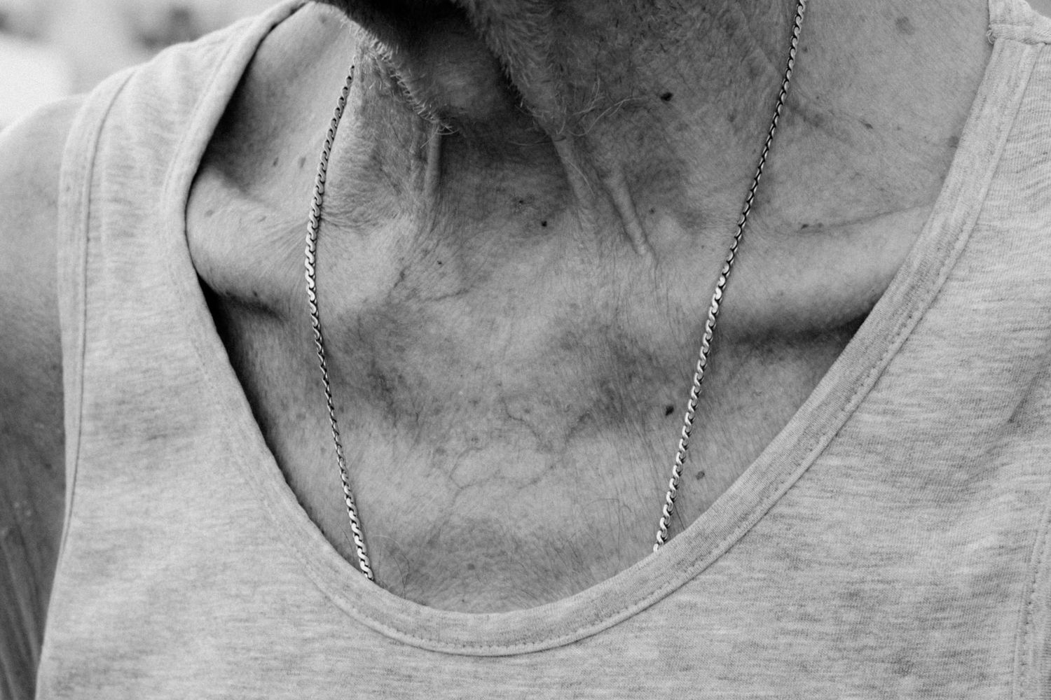 Close-up black and white photo of a gray tank top neckline with a thin silver chain necklace.