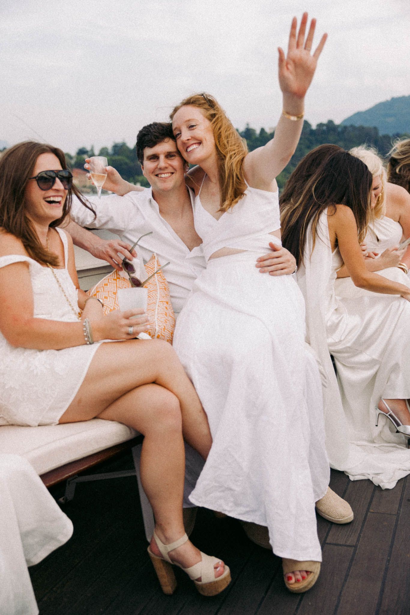 A group in white outfits laughing and having fun during a casual photoshoot on a wooden deck.