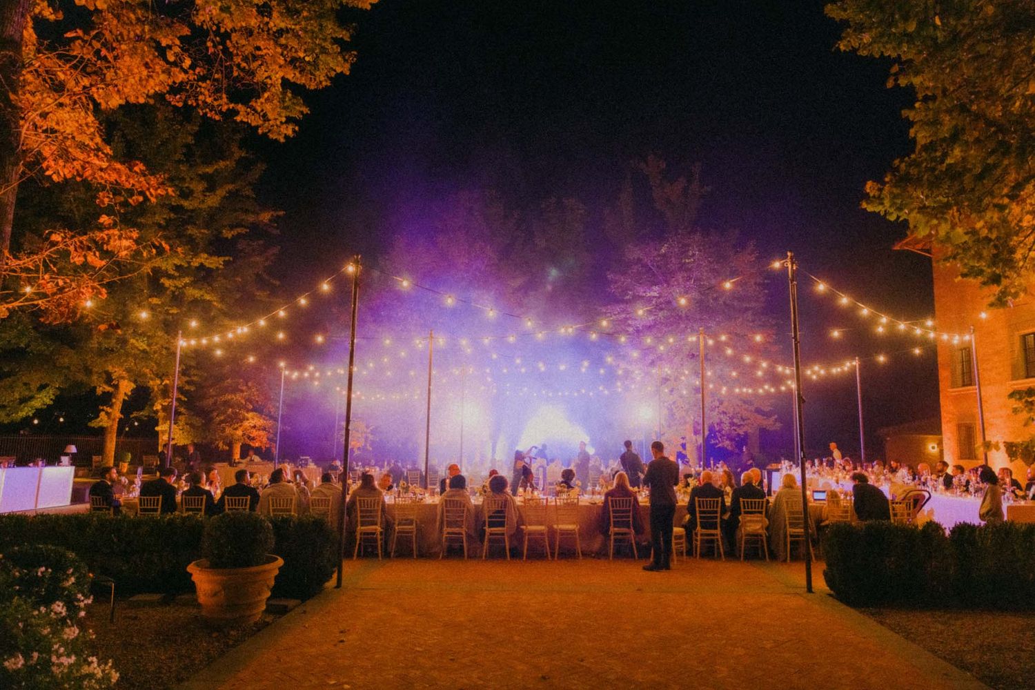 String lights illuminate an outdoor evening festival with purple and orange lighting creating a magical atmosphere.