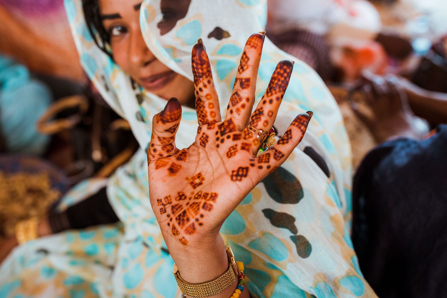 Close-up of a hand decorated with intricate henna designs against light blue fabric.