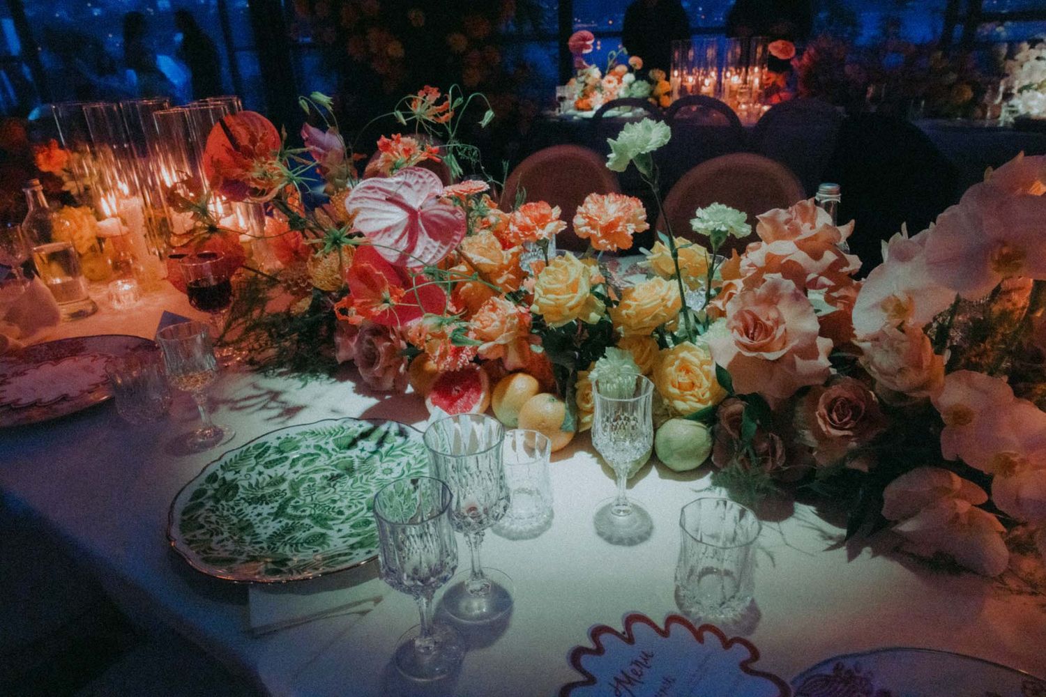 Romantic wedding reception table setting with pink and orange floral arrangements and glowing candlelight.