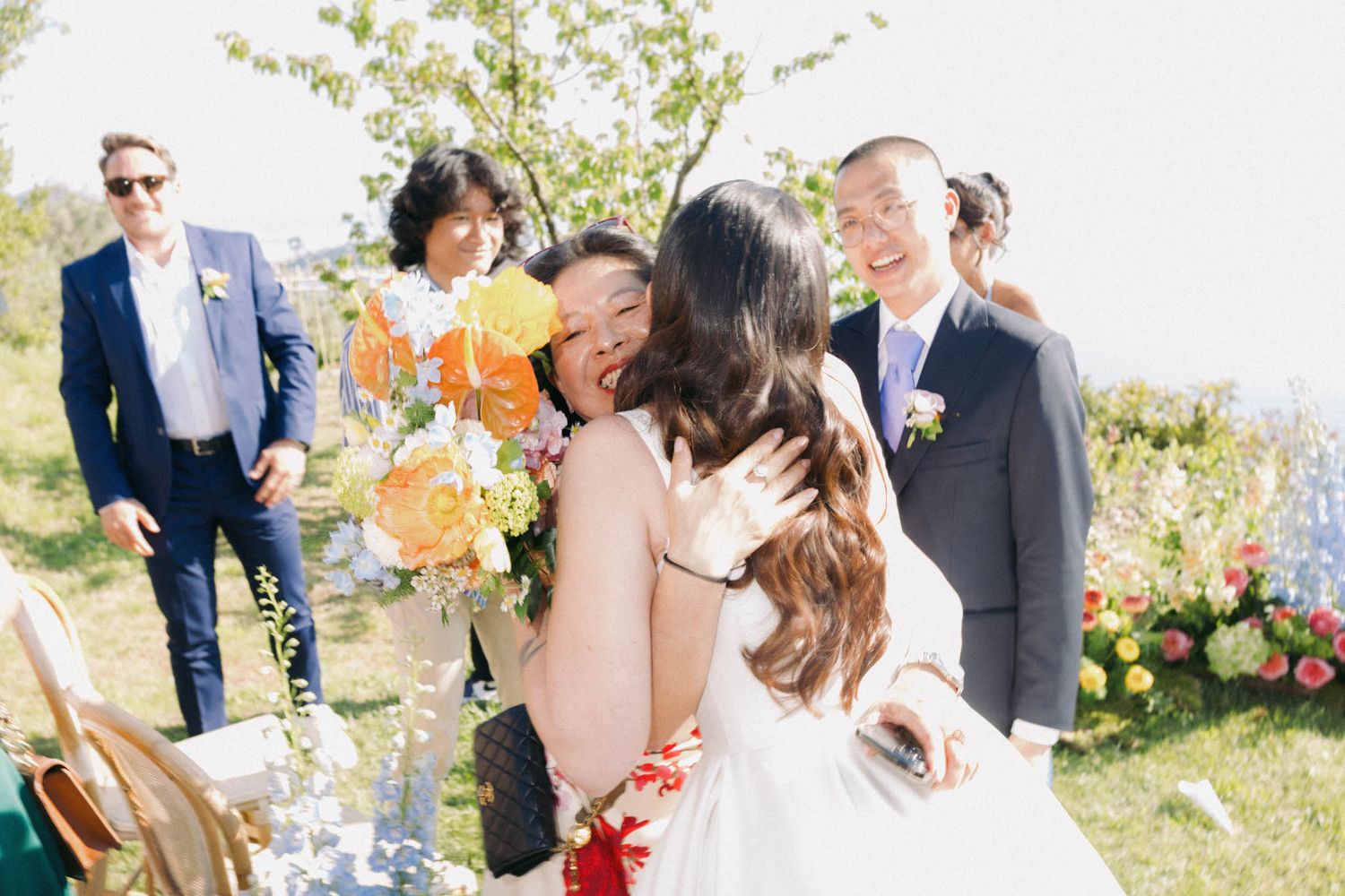 Wedding party celebrates with confetti toss in garden setting with vibrant floral arrangements.
