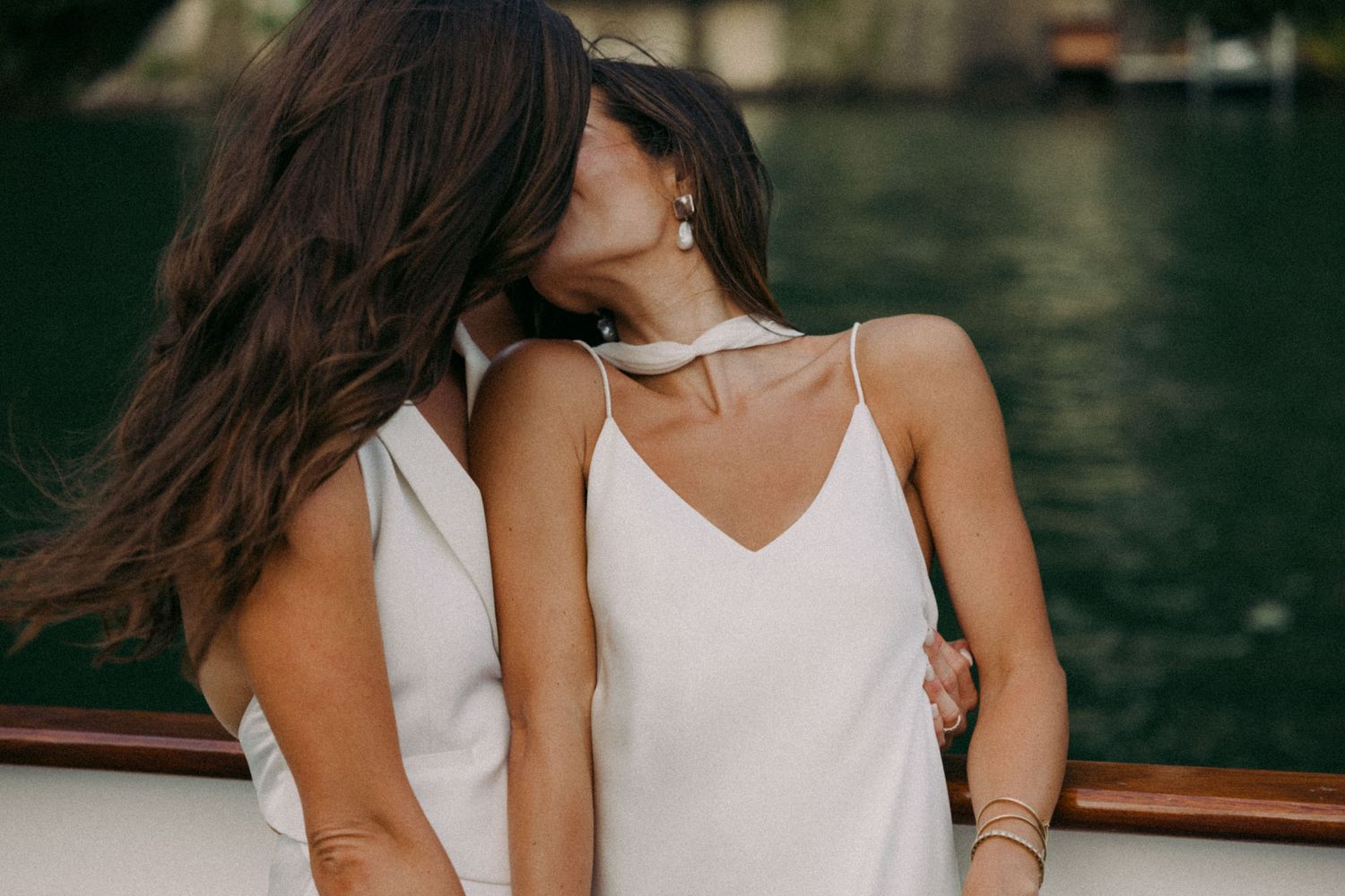 Couple in white outfits embracing and laughing during a romantic photoshoot near water.