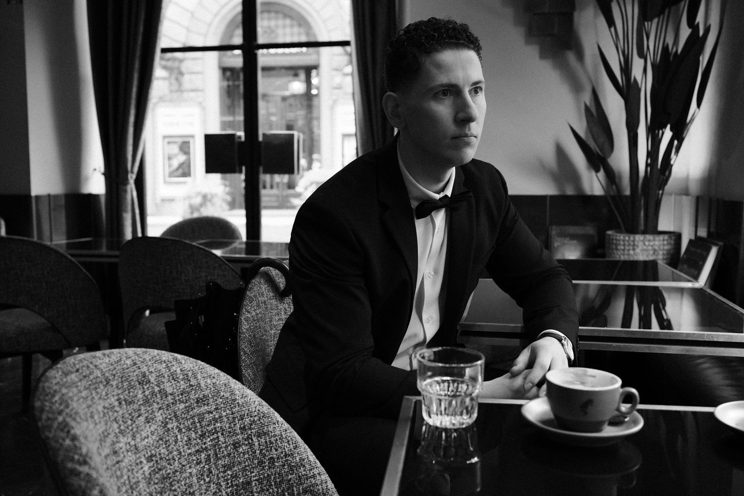 A person sits in a dimly lit cafe with a laptop and coffee cup on the table in front of them.