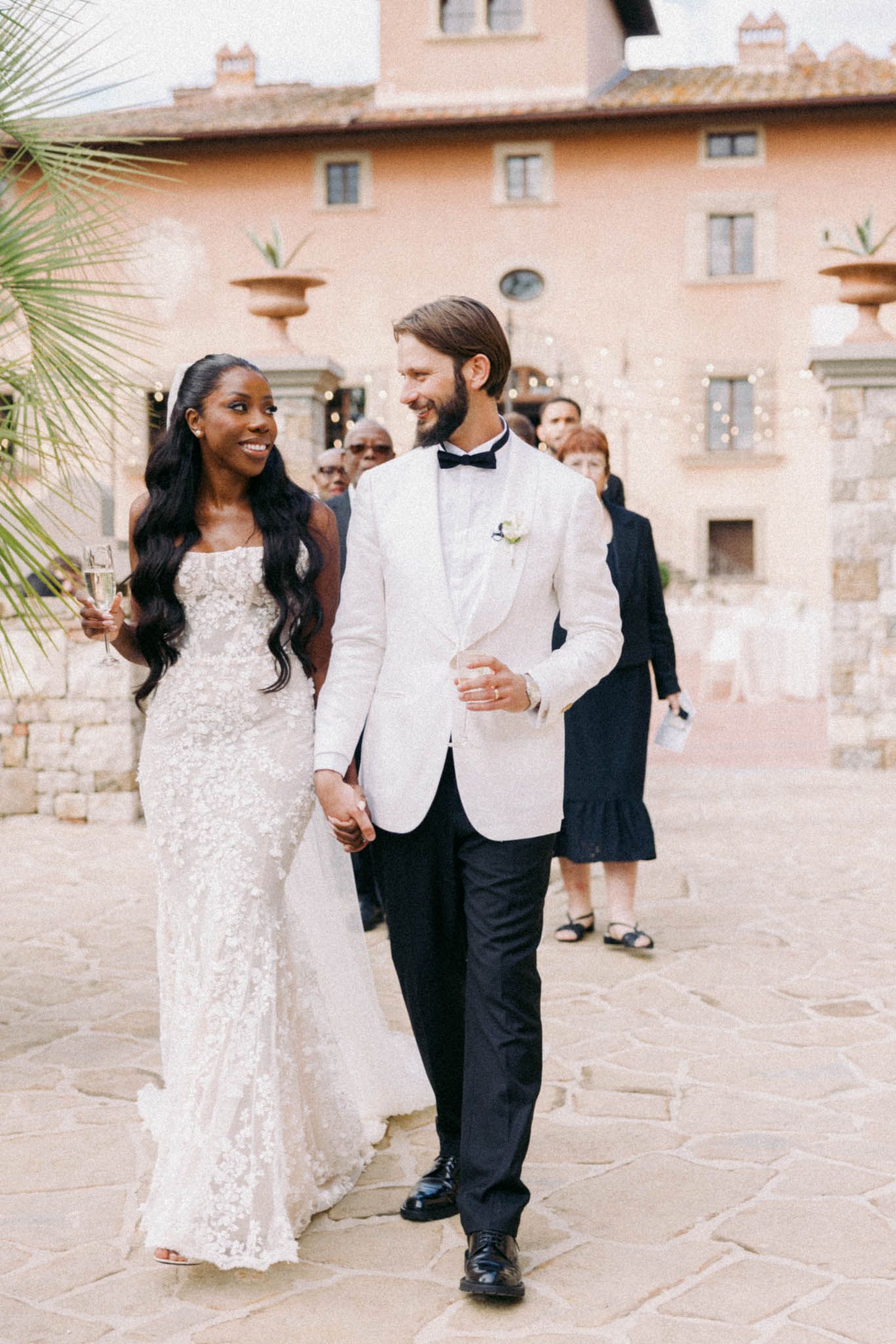 A couple shares joyful moments in their wedding attire at a rustic stone venue with peach-colored walls.
