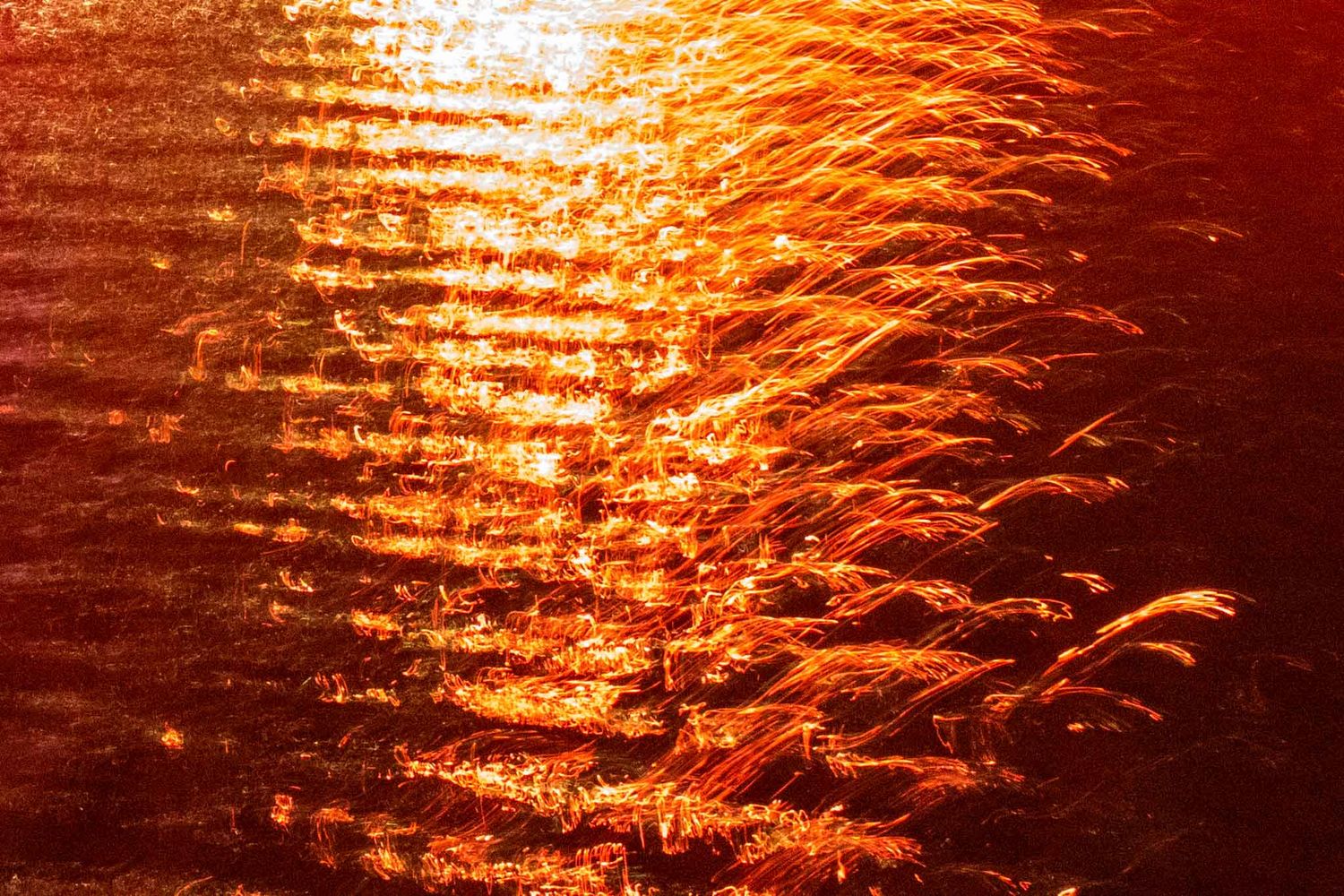 Golden sunlight reflects off rippling water creating a shimmering orange pattern at sunset.