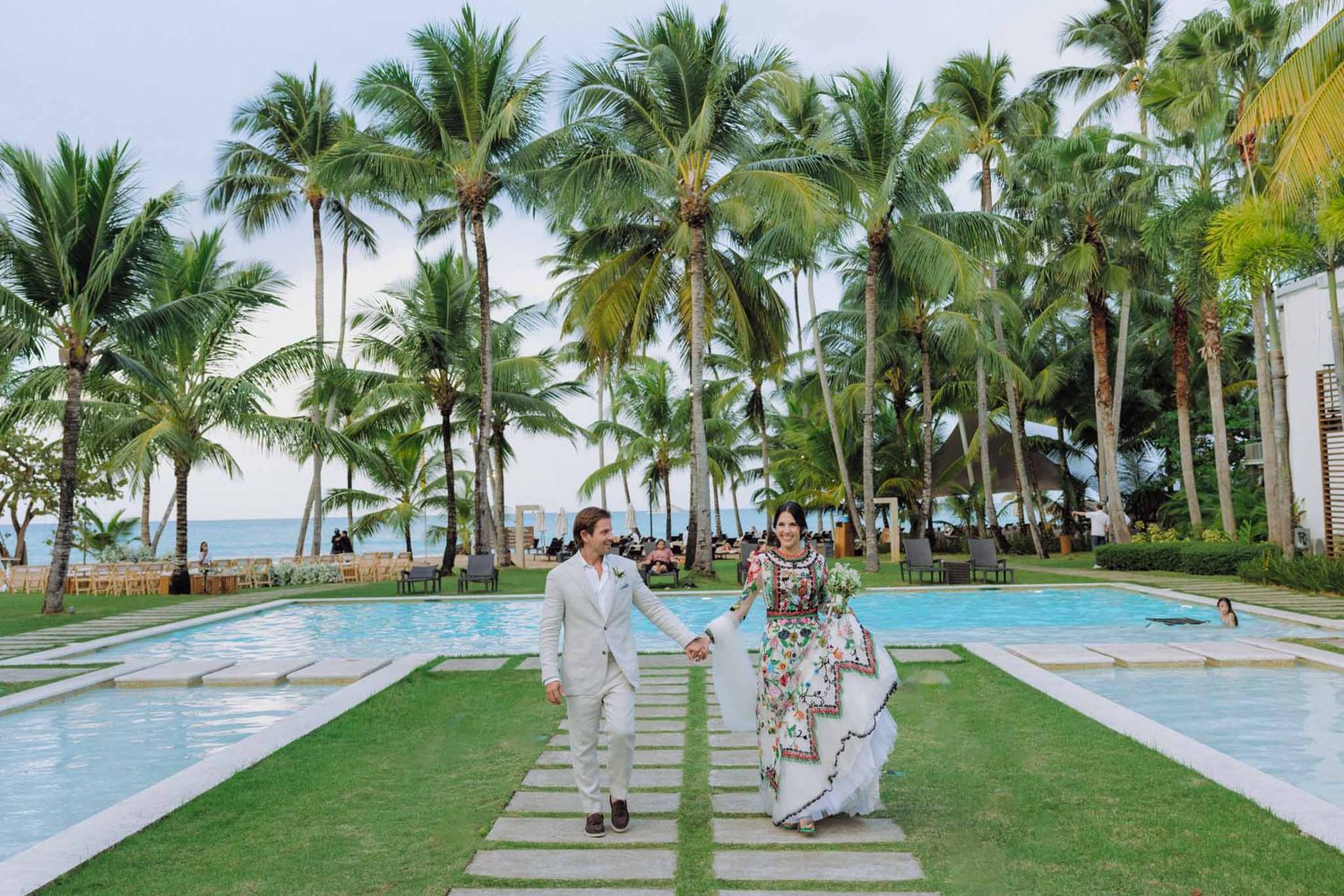 A scenic beachfront wedding ceremony setup with white chairs and palm trees along a tropical coastline.